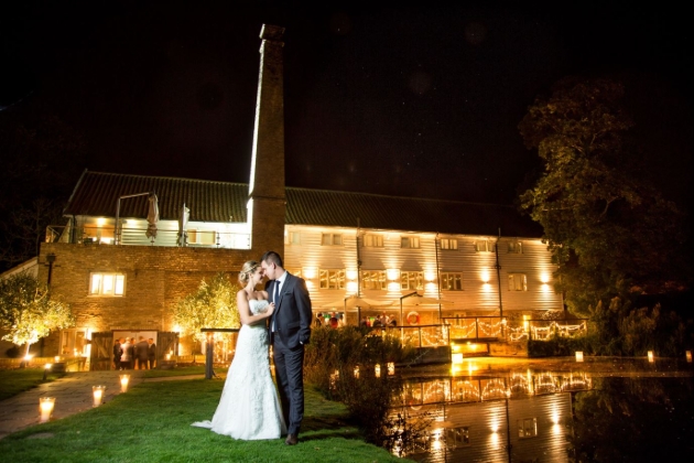 Tuddenham Mill at night, couple standing in from of mill by river 