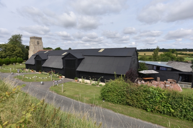 Alpheton Hall Barns aerial view of the black barns church in the background and fields