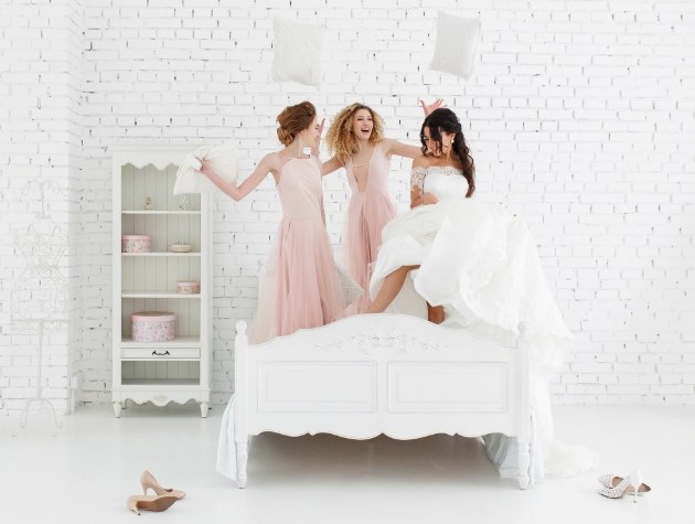 bride and bridesmaids on bed jumping happy