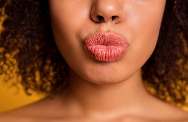Cropped close up photo of lipstick lips, curly brunette hairdo, isolated on yellow background