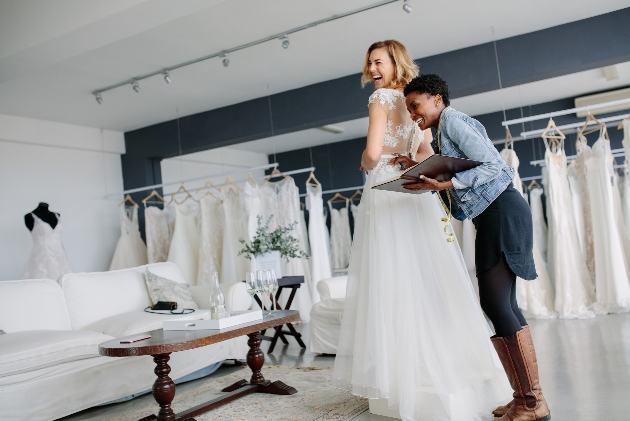 woman in a dress shop trying on a wedding dress with the shop assistant