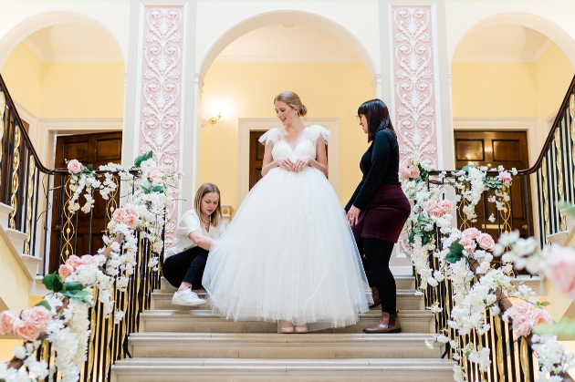 bride in a wedding dress walking down the stairs with the help of two planners