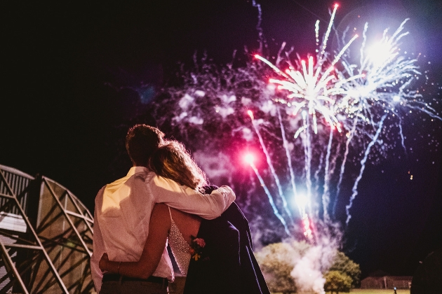 a bride and groom at night standing outside looking up at fireworks