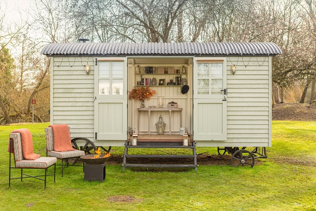 green shepherd's hut in a field with chairs outside