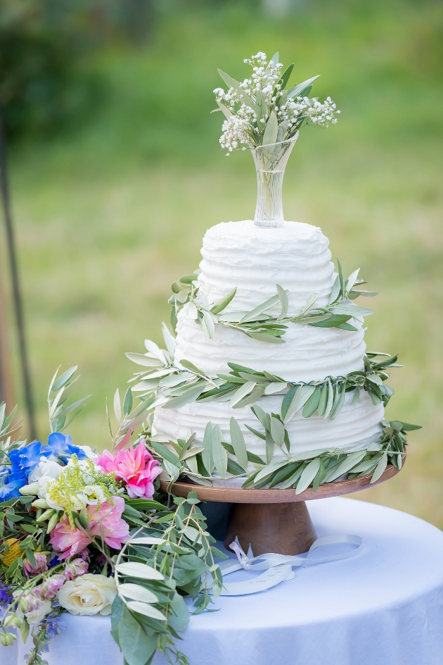 White wedding cake on stand wrapped with flowers