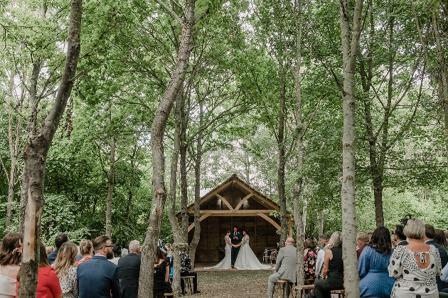 bride and bride standing under wooden structure in woods