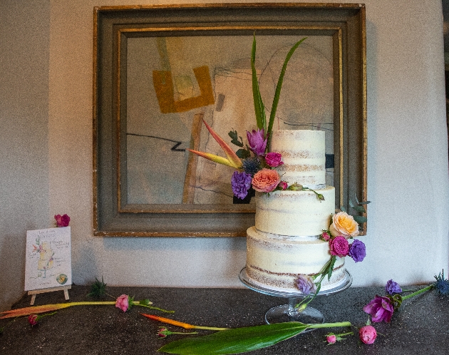 naked cake with exotic flowers next to mini easel of painted cake