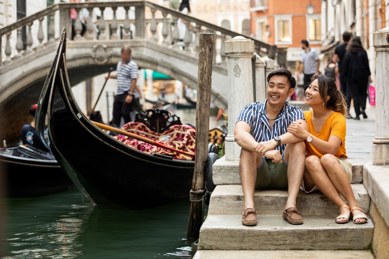 couple sat on steps in italy with gondola going down river