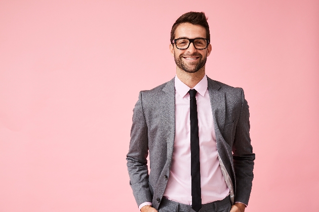 Man smiling wearing a grey suit in a pink studio