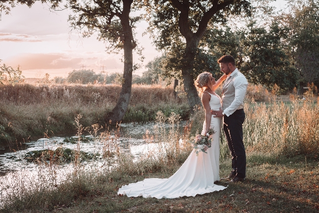 Bride and groom embracing next to a lake