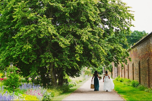 bride and bridesmaid walking on a path down the edge of a walled garden