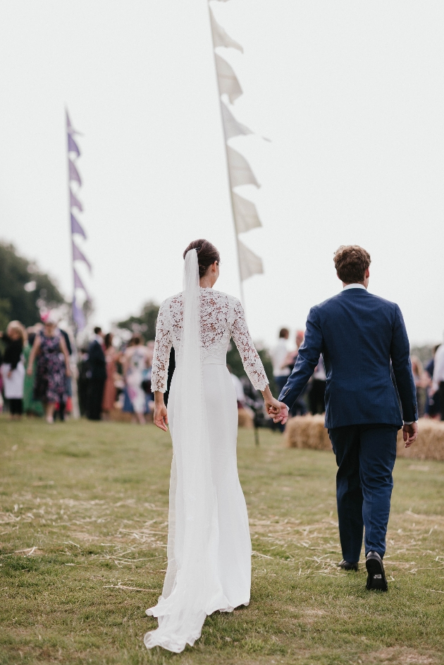bride and groom walking away from camera hand in hand on field