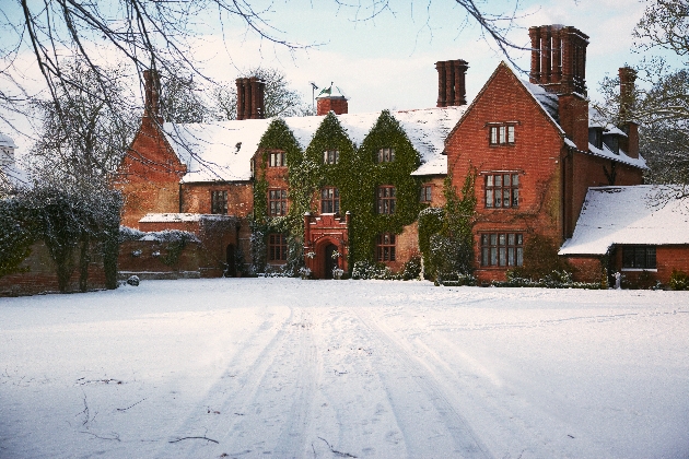 The exterior of a red manor house surrounded by snow