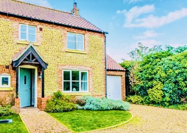 A yellow building with a driveway and front garden
