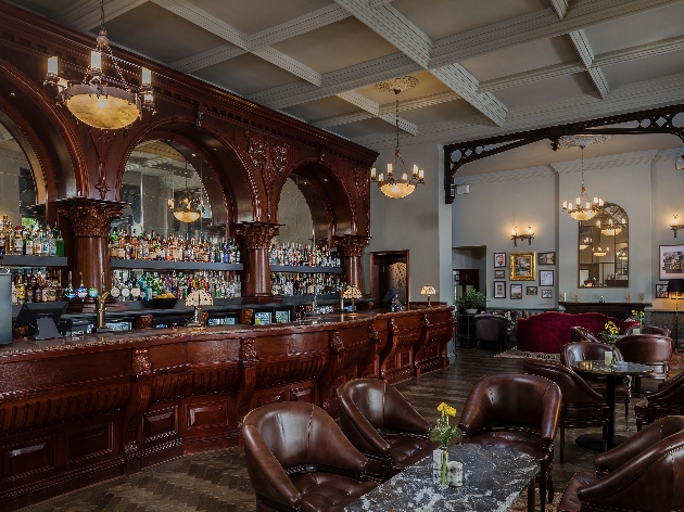 A bar made from brown wood with tables and chairs close by