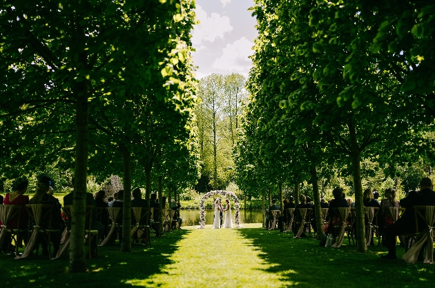 Two women getting married under an arch surrounded by trees