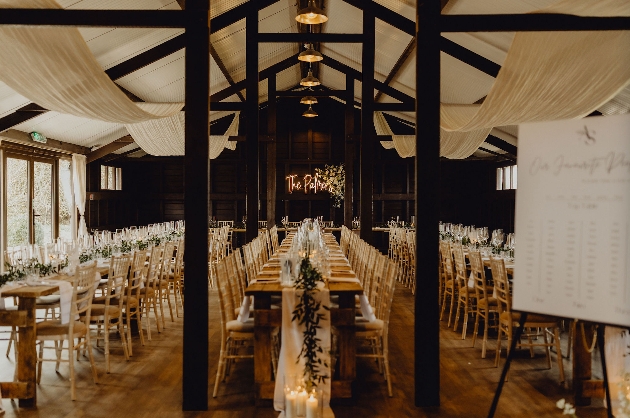 Long tables set up inside a barn decorated with flowers and white fabric