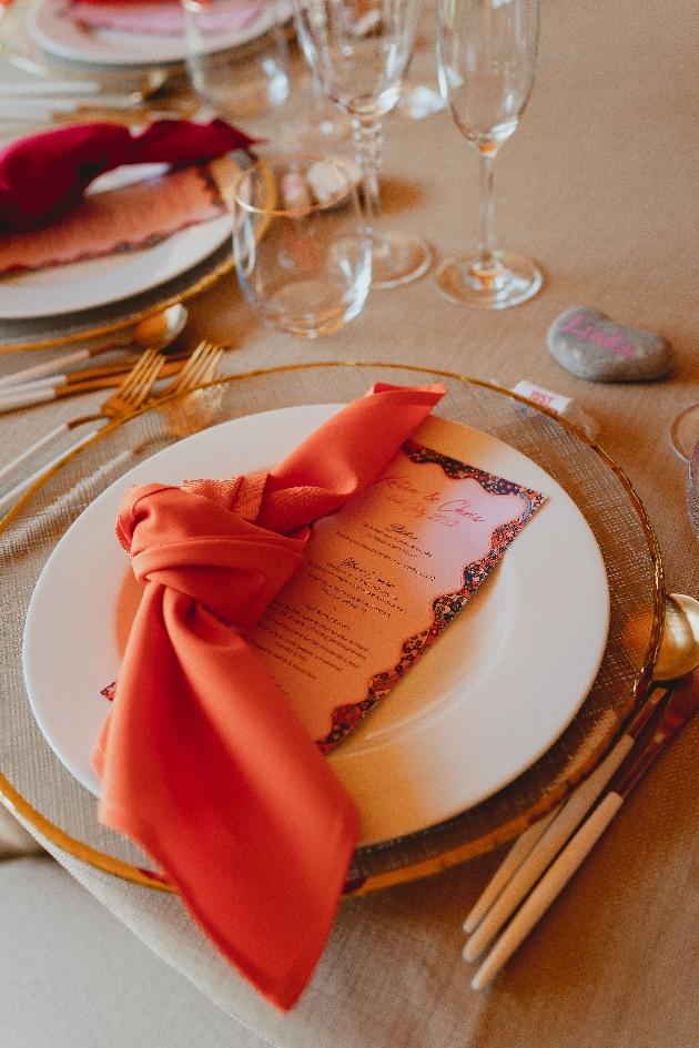 A table with a white plate with a red napkin and pink invitation in the centre of it
