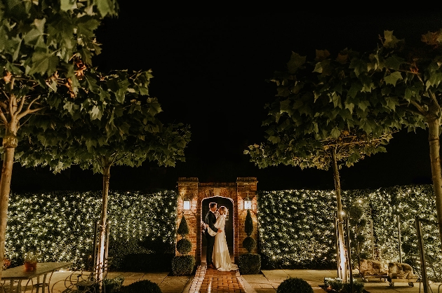 A bride and groom embracing in a garden light with fairylights