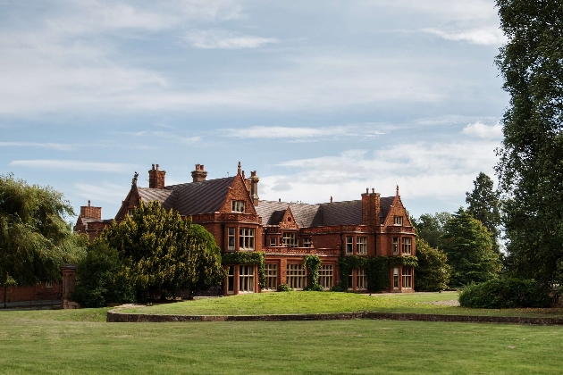 The exterior of a large brick manor house surrounded by trees and grass