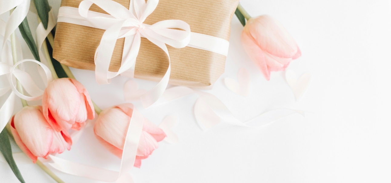 A craft paper wrapped present with white bow and tulips on white table