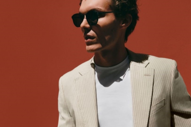 man in light suit with t-shirt underneath posing in front of a red wall