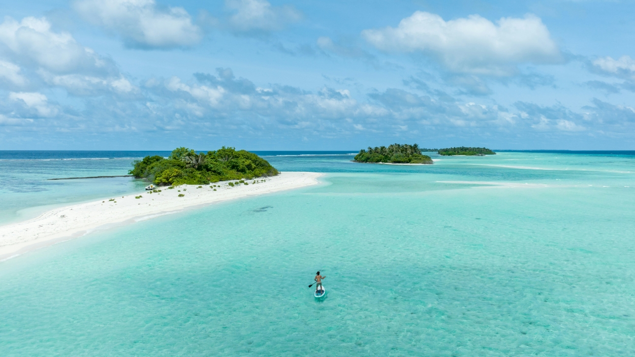 Maldives, person on paddle board in water, aerial view