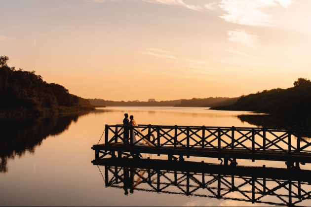 A bride and groom standing on the end of a dock as the sun sets